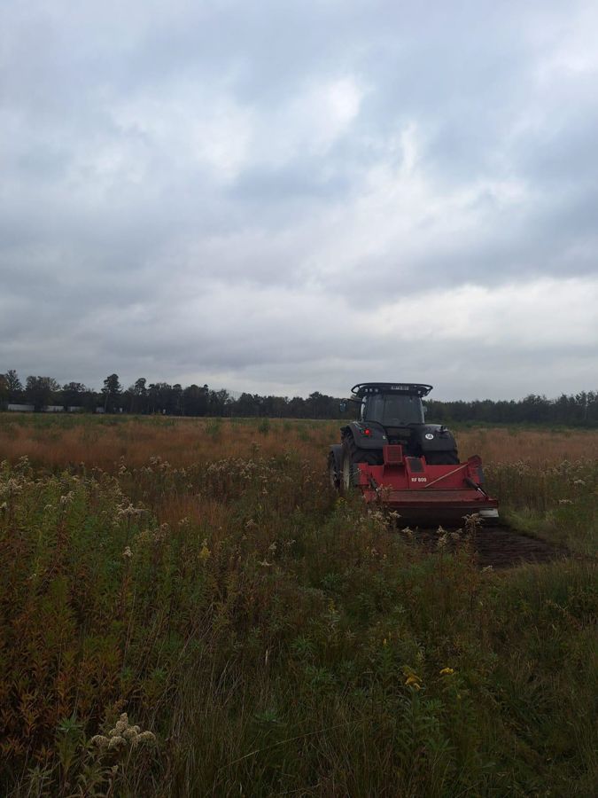 An einem bewölkten Tag fährt ein Traktor durch eine Wiese.