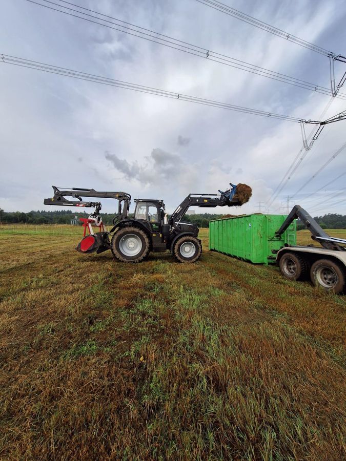 Ein Traktor lädt auf einem Feld Heu auf einen Anhänger.