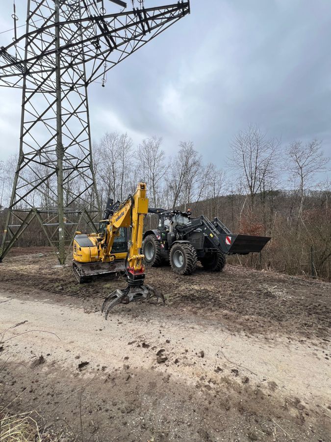 Ein gelber Bagger und ein schwarzer Traktor stehen nebeneinander auf einem Feldweg.