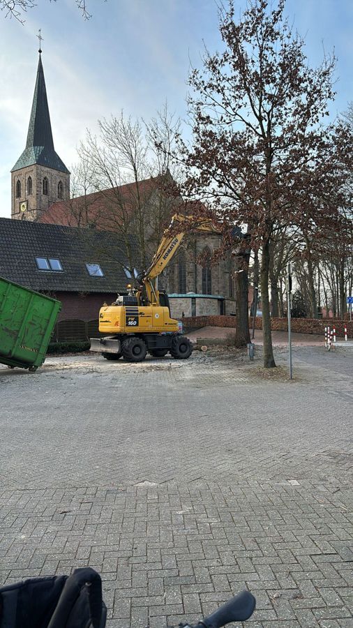 Ein gelber Bagger fährt eine Ziegelsteinstraße vor einer Kirche entlang.
