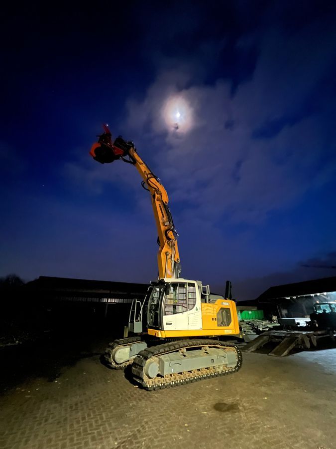 Ein gelb-weißer Bagger steht nachts auf einem Parkplatz.