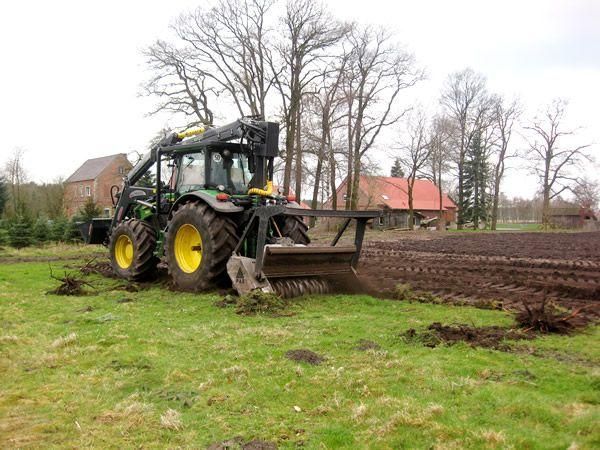 Ein Traktor pflügt ein Feld, im Hintergrund ist ein Haus zu sehen.