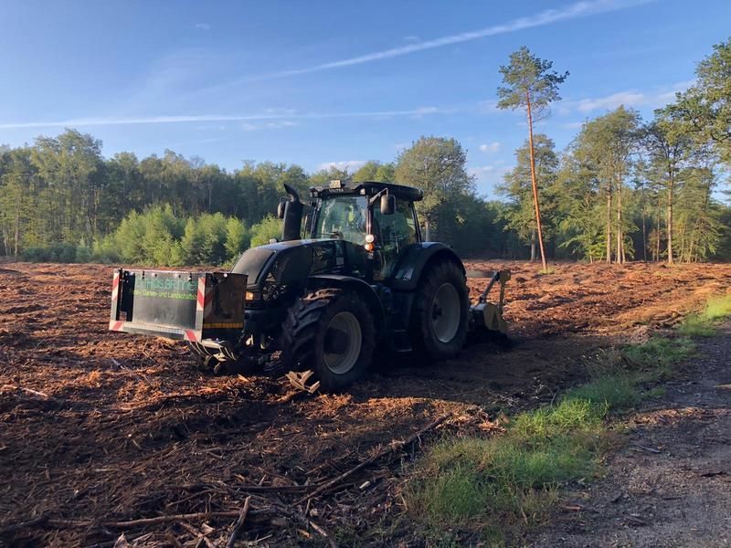 Ein Traktor pflügt ein Feld, im Hintergrund sind Bäume zu sehen.