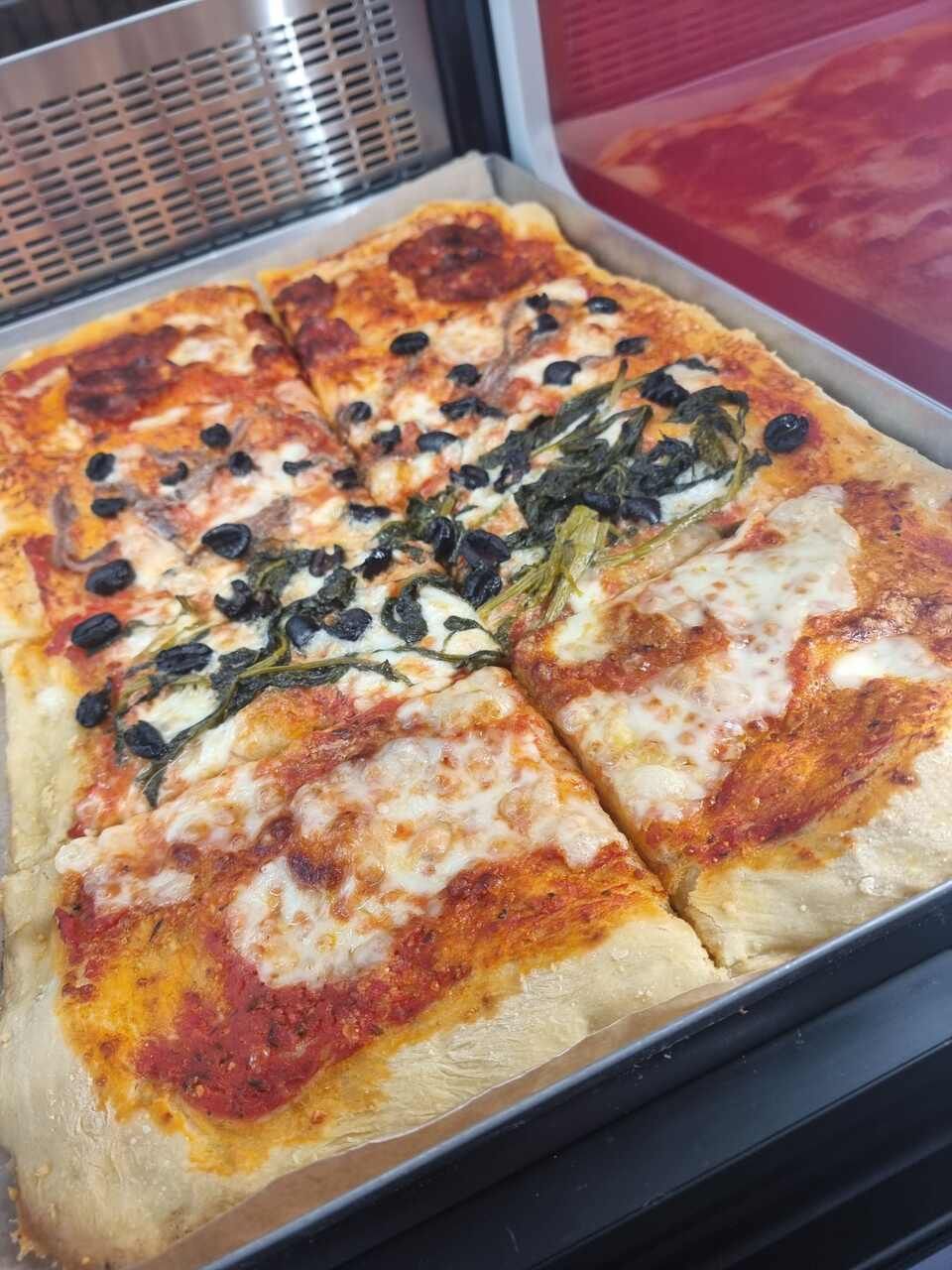 Une pizza avec des olives et des épinards est dans une boîte