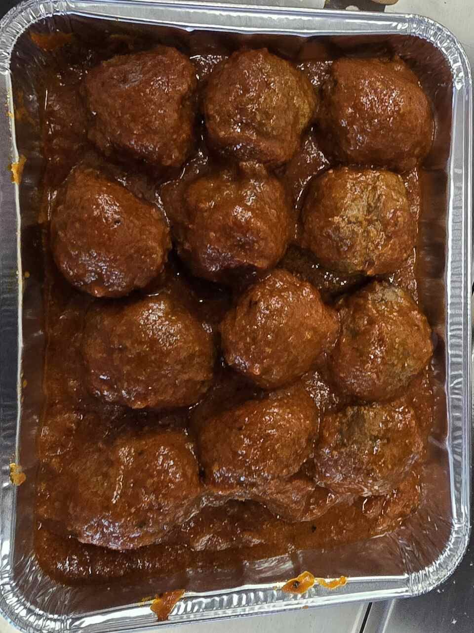 Un récipient en aluminium rempli de boulettes de viande en sauce sur une table.