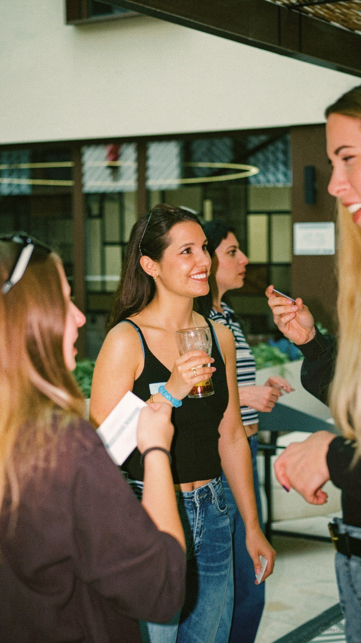 Personas socializando en un evento en un espacio cerrado, sosteniendo bebidas y charlando cerca de una puerta.
