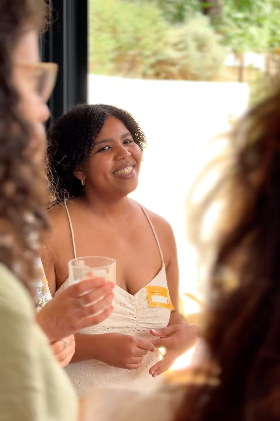 Mujer sonriendo y sosteniendo una bebida en una reunión informal al aire libre.