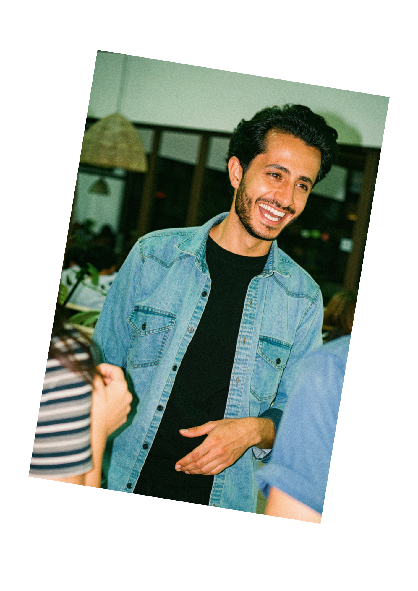 Hombre sonriente con chaqueta vaquera en una reunión informal en un espacio cerrado, fotografiado con una ligera inclinación.