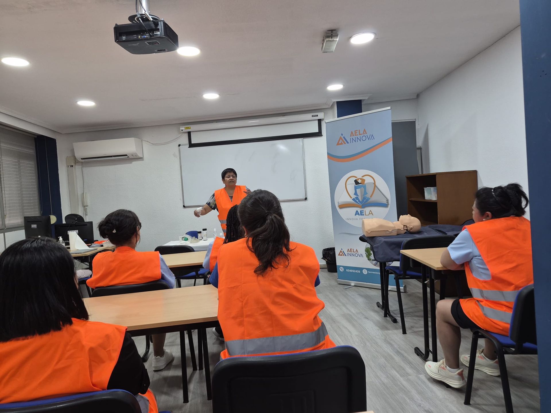 Instructor presenta “Formación Sociosanitaria” a estudiantes sentados en un aula luminosa.