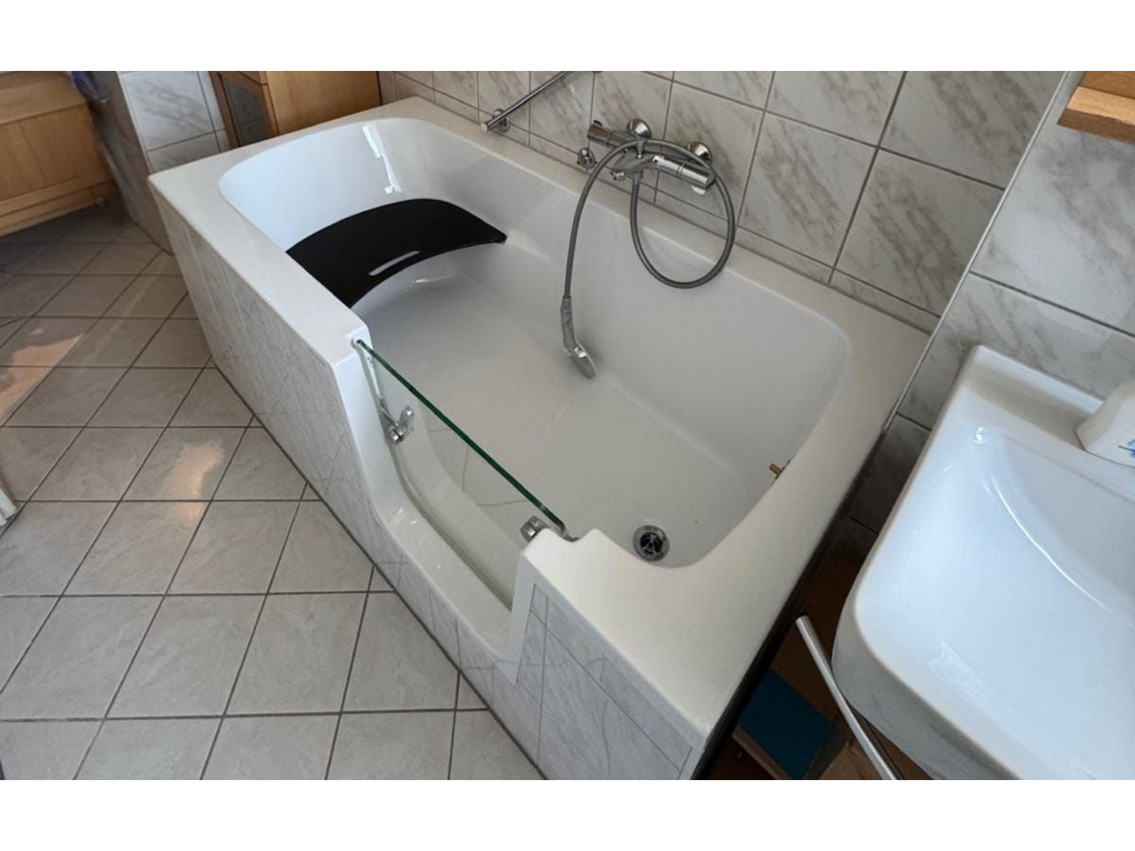 Moderne Badewanne mit grau weißen Fliesen und Glasausbuchtung