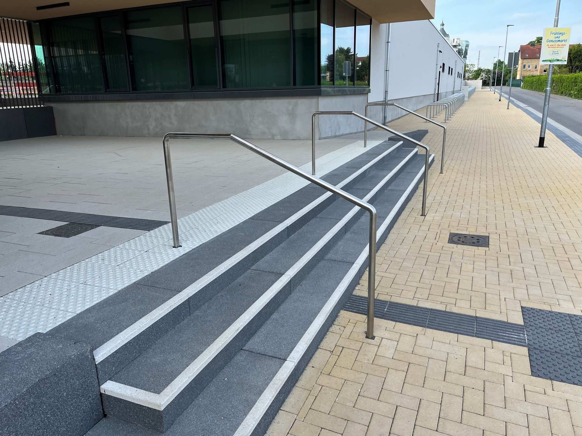 Betontreppe mit Metallhandlauf neben einem Gehweg und dem Gebäudeeingang.