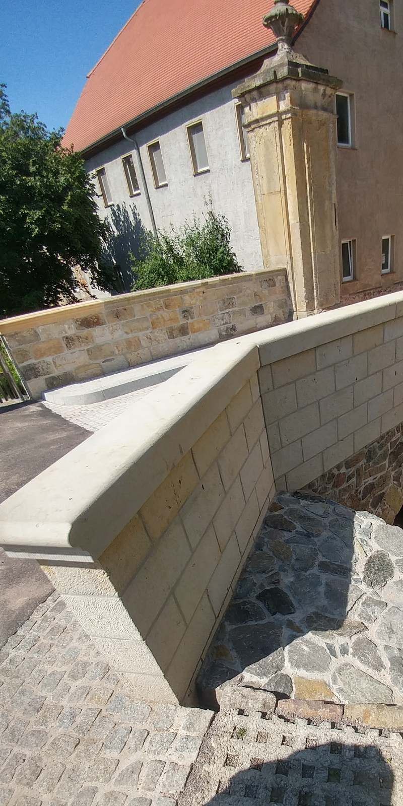 Steinweg neben einem weißen Gebäude mit rotem Ziegeldach und niedriger Steinmauer im Sonnenlicht