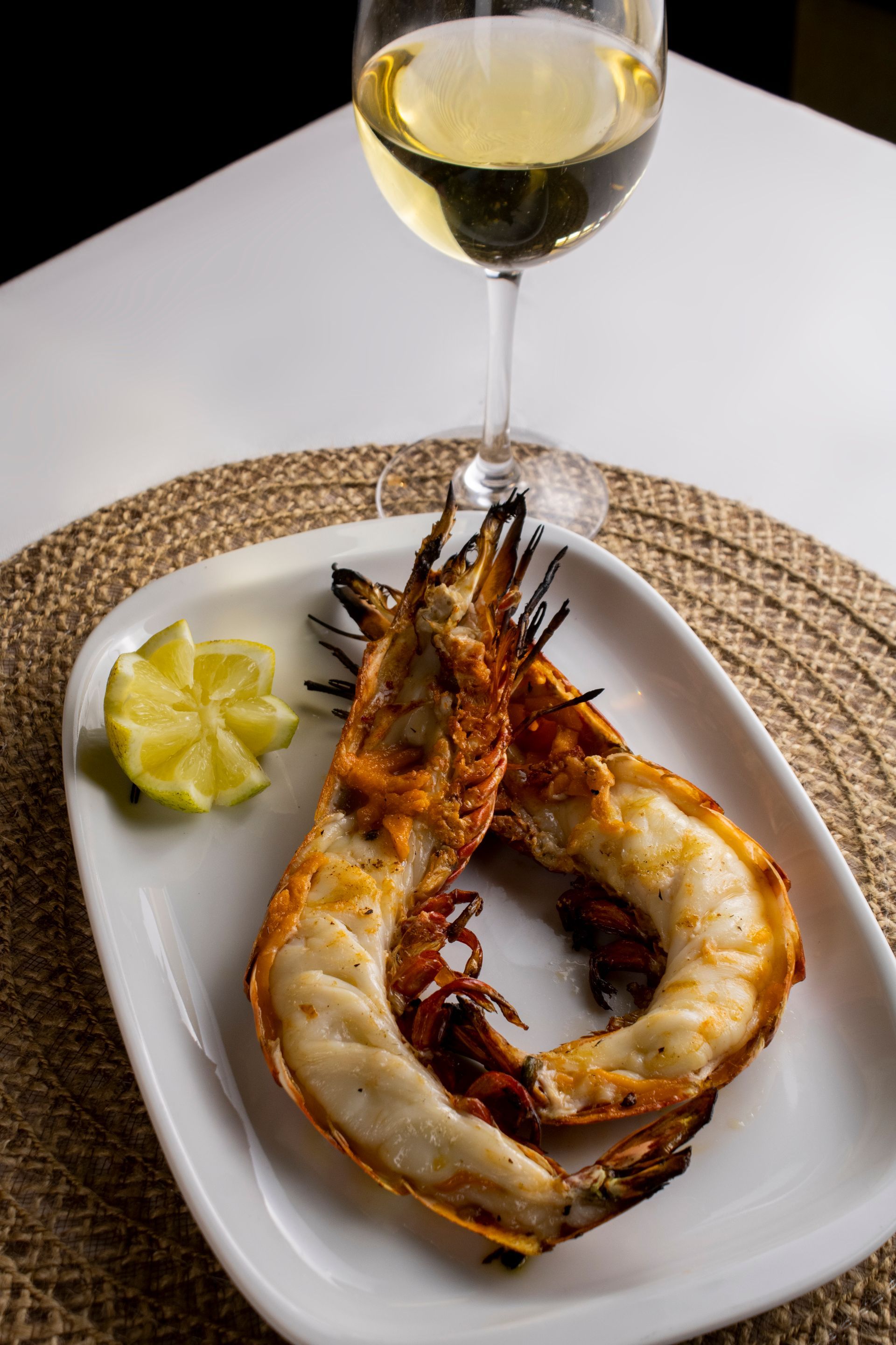 Camarão grelhado em um prato branco com fatia de limão e taça de vinho branco.
