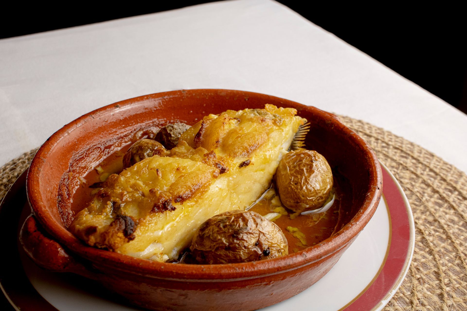 Bacalhau assado com batatas em uma tigela de cerâmica marrom.