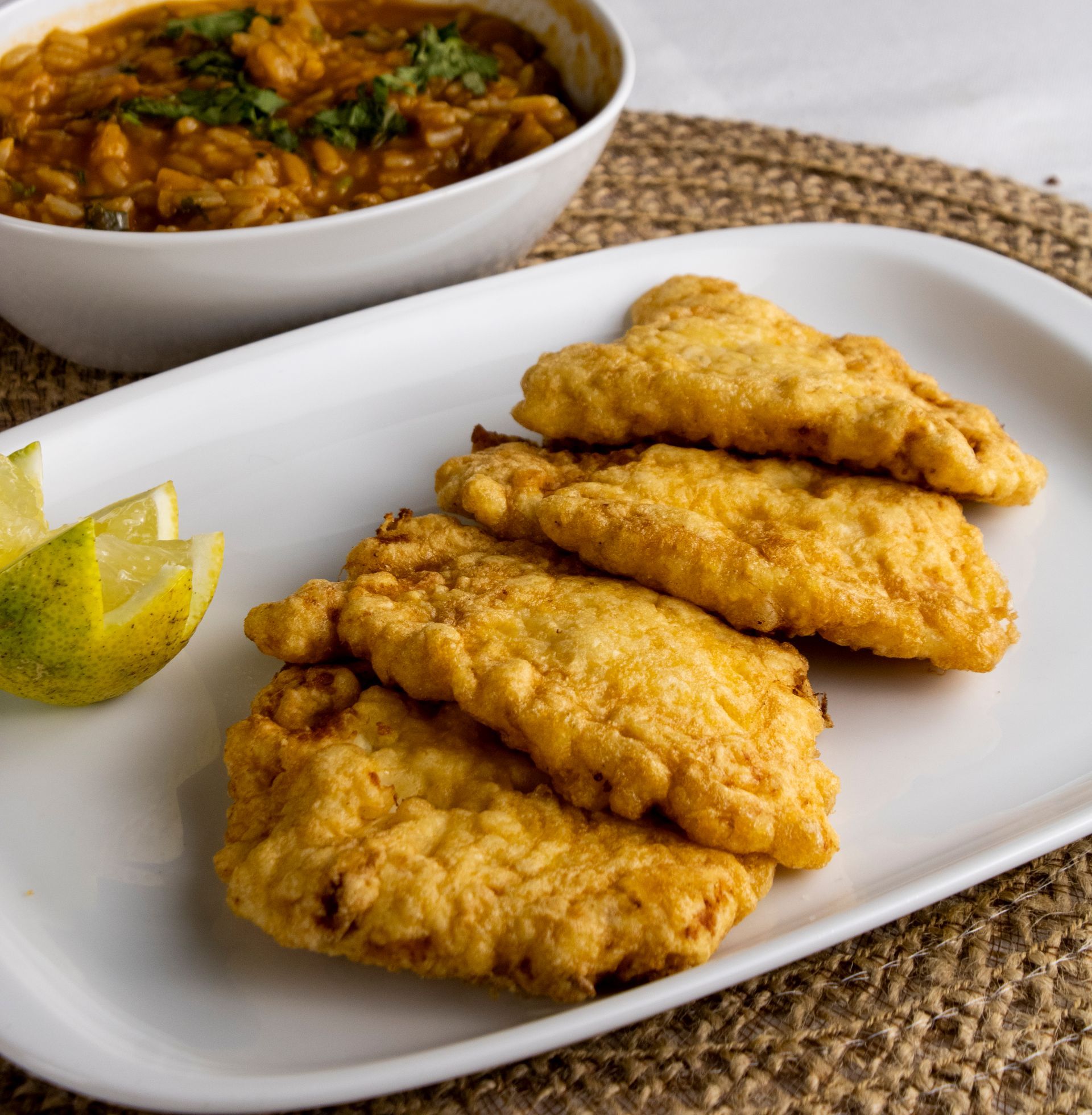 Filés de peixe frito em prato branco com tigela de ensopado e fatias de limão.