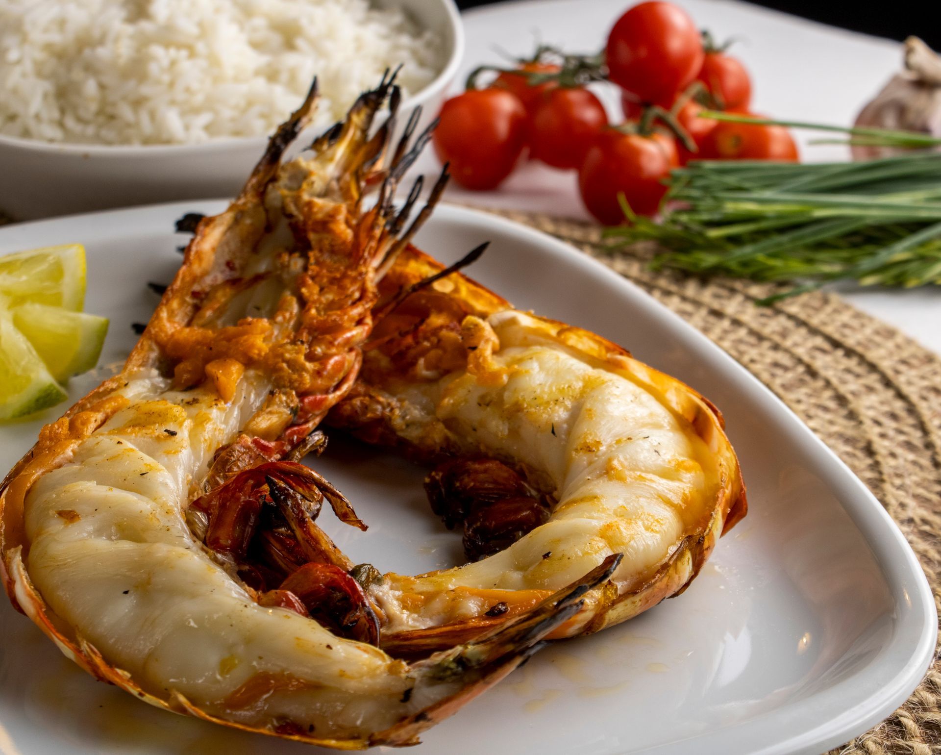 Camarões gigantes grelhados em prato branco com arroz, tomate e limão.