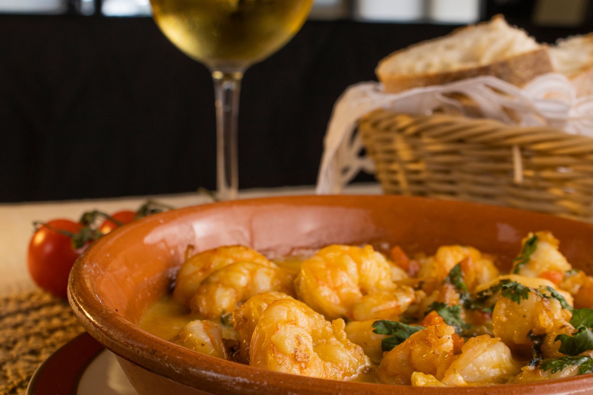 Camarão scampi em um prato de terracota, vinho branco, cesta de pão, tomates.