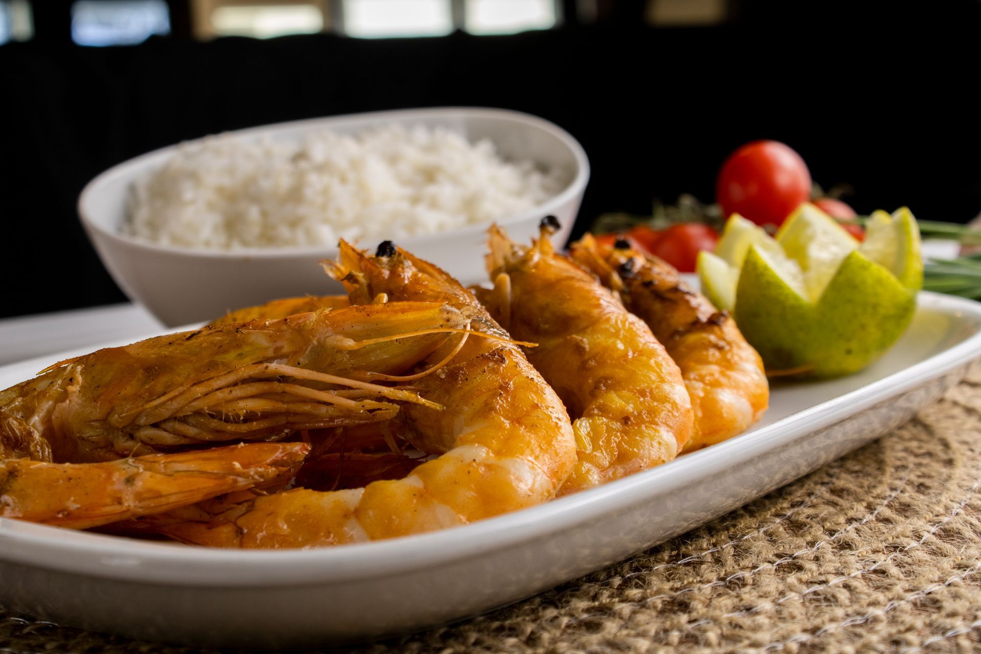 Camarão grelhado em um prato branco, servido com arroz, tomate, limão e cebolinha.