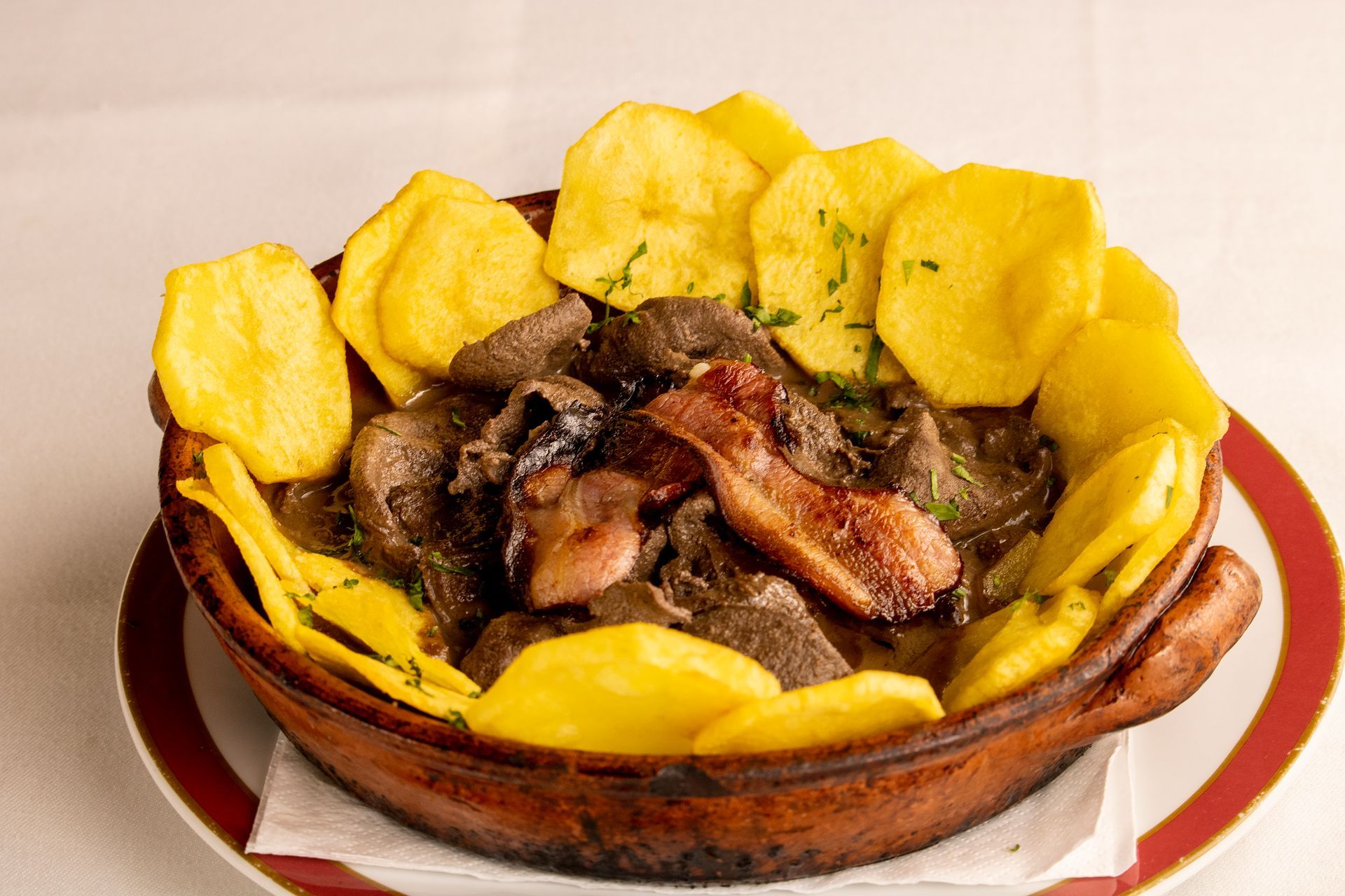 Prato farto de carne escura, bacon e batatas fritas em uma tigela marrom.