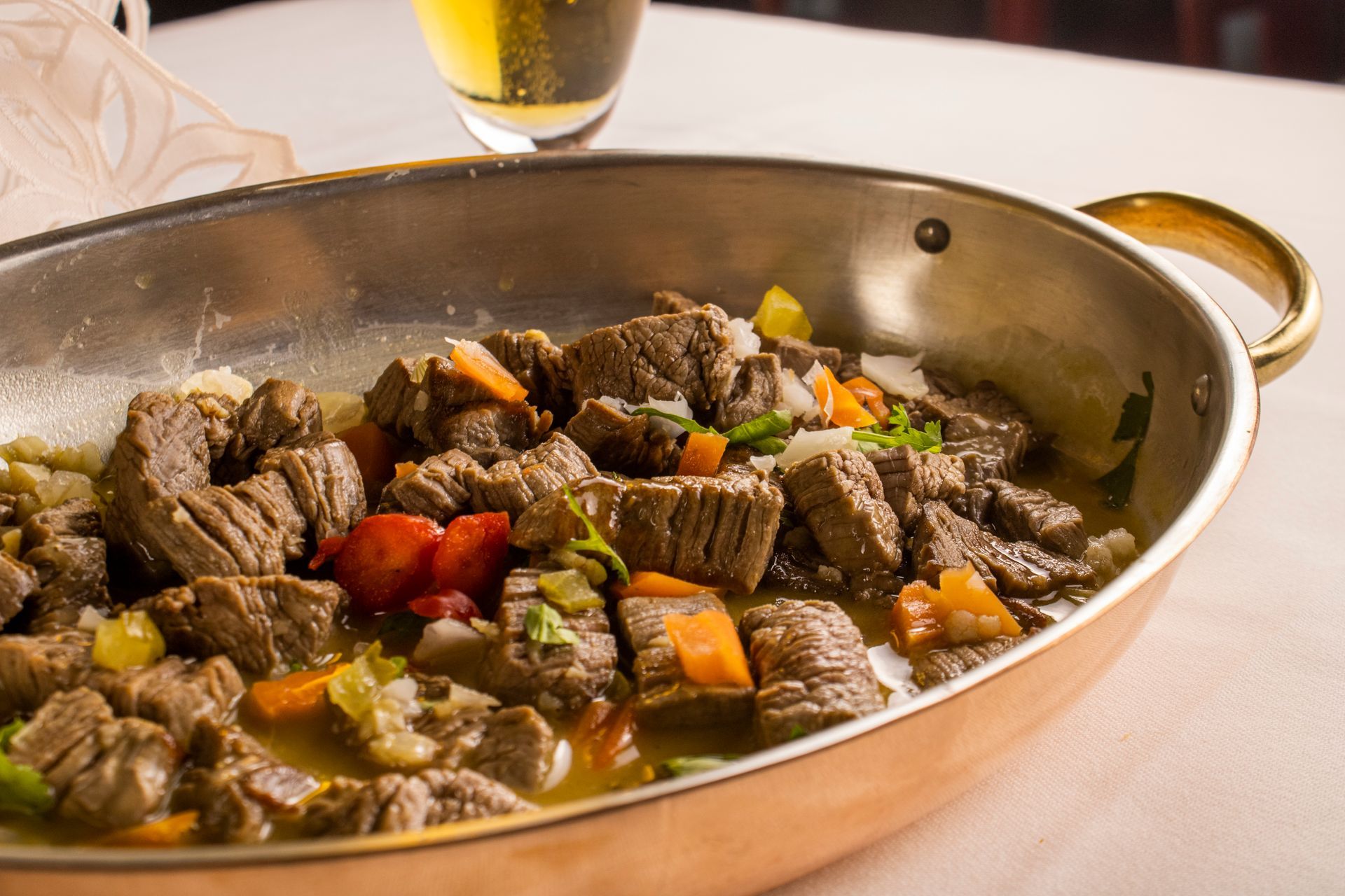 Ensopado de carne com legumes em uma panela de cobre, copo de cerveja ao fundo.