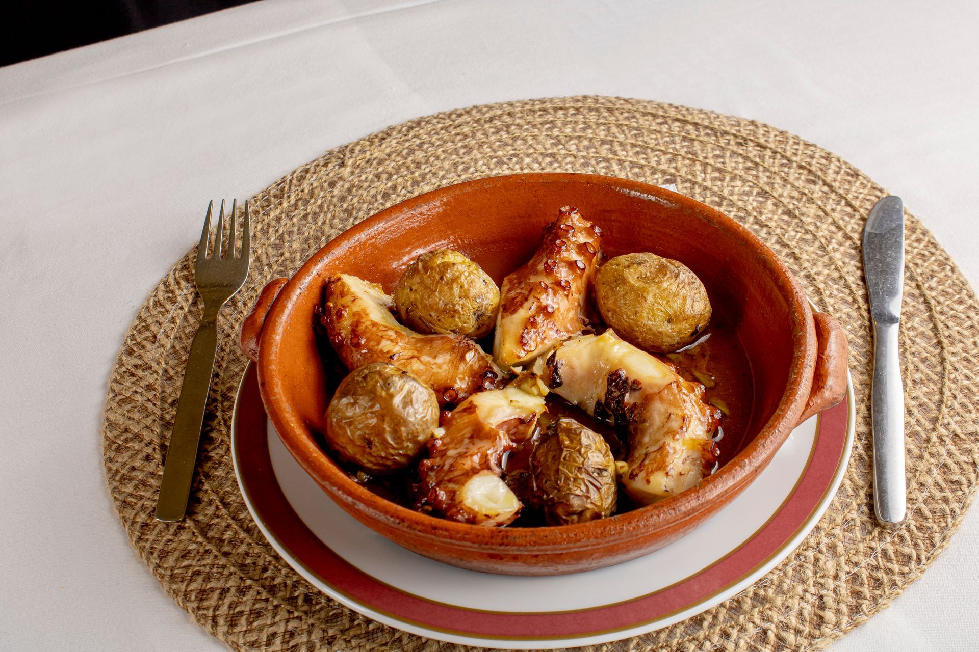 Ensopado de bacalhau e batatas servido em uma tigela rústica de terracota com talheres sobre uma esteira de vime.