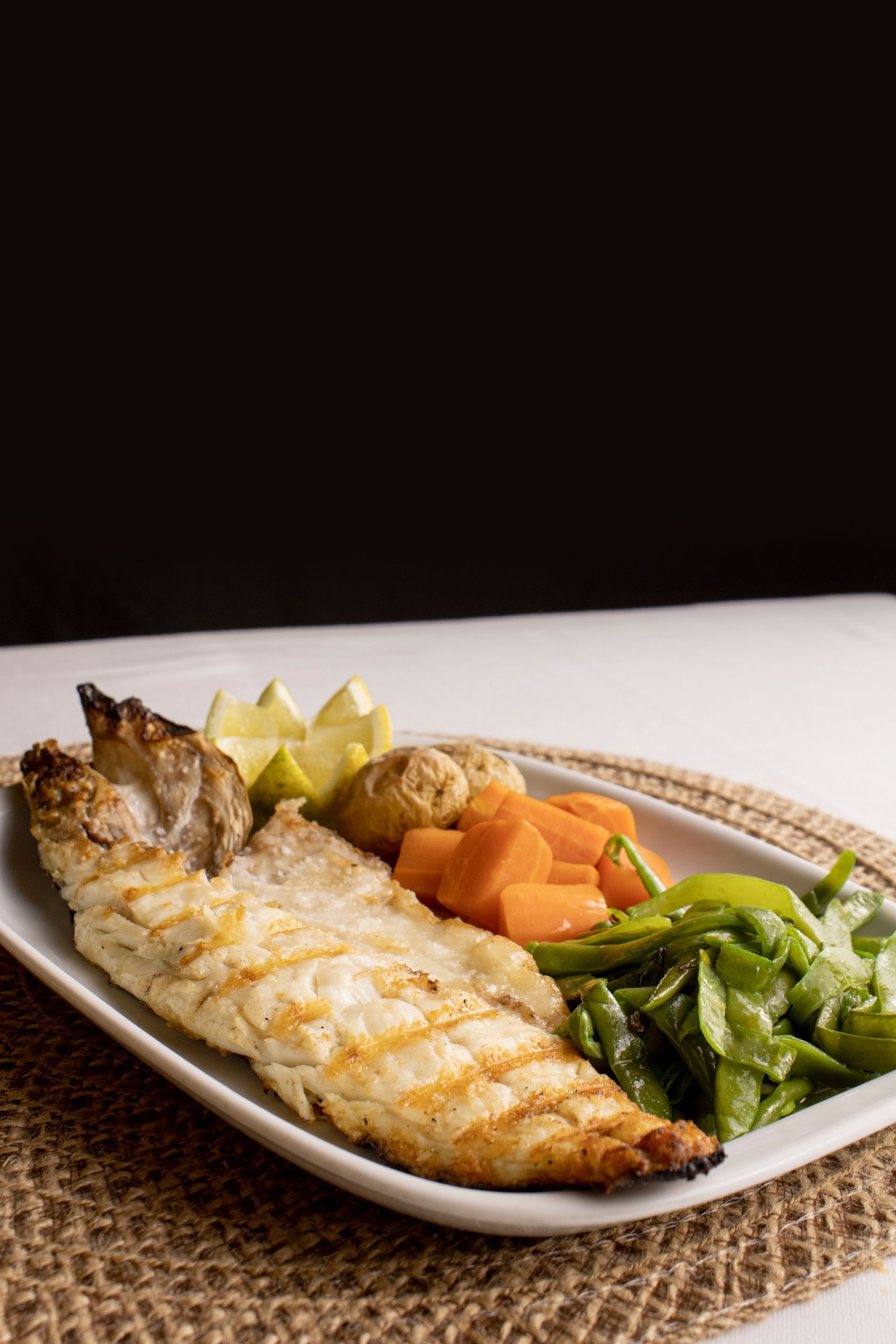 Peixe grelhado com acompanhamentos de vegetais em um prato.