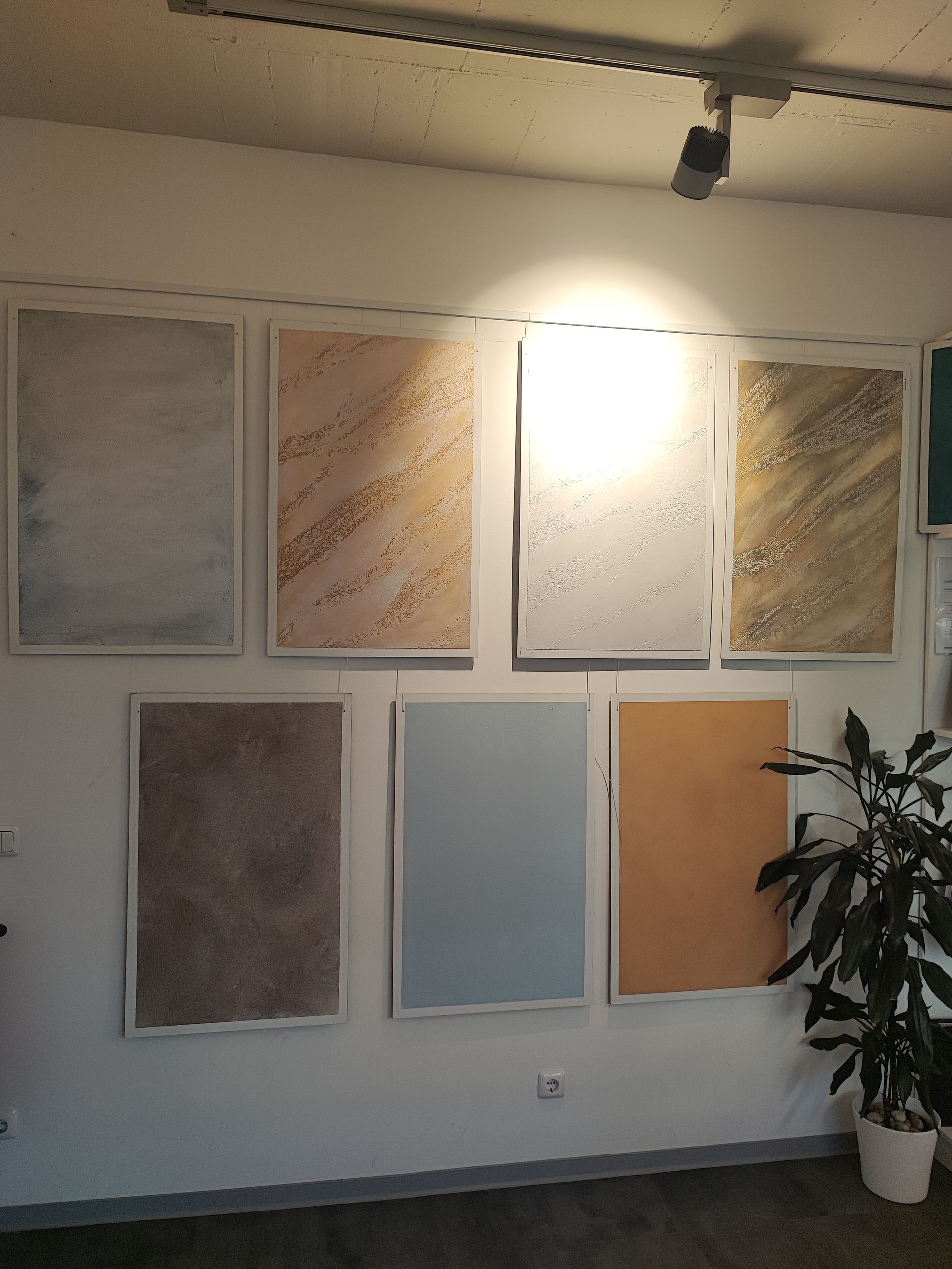 In einem Ausstellungsraum werden Muster von strukturierten Wandbeschichtungen präsentiert. Verschiedene Farben und Muster werden in gerahmten Tafeln gezeigt.