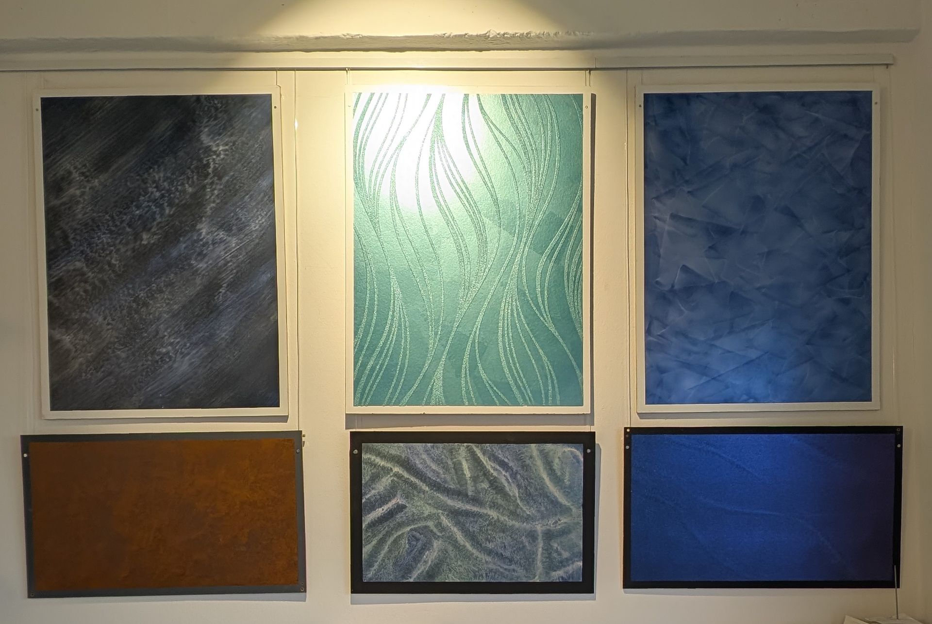 Sechs gerahmte abstrakte Kunsttafeln in Blau-, Grün- und Brauntönen hängen an einer weißen Wand.