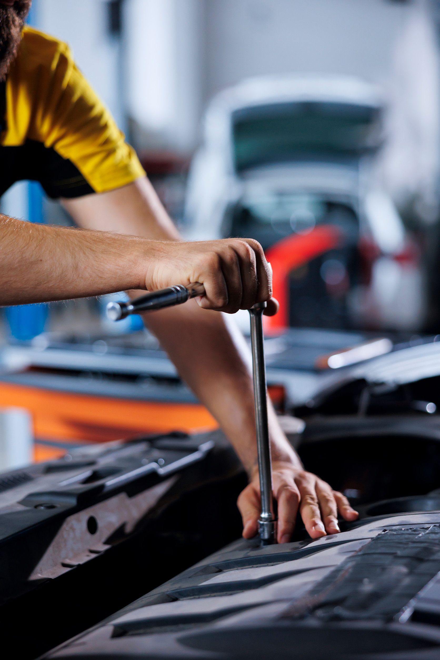 Un hombre está trabajando en el capó de un coche con una llave inglesa.