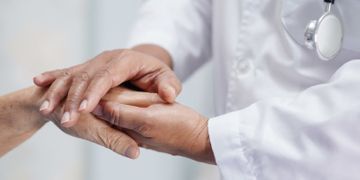 Un médico sostiene la mano de una mujer mayor.