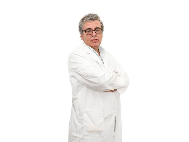 Un hombre con bata de laboratorio y gafas está de pie con los brazos cruzados.