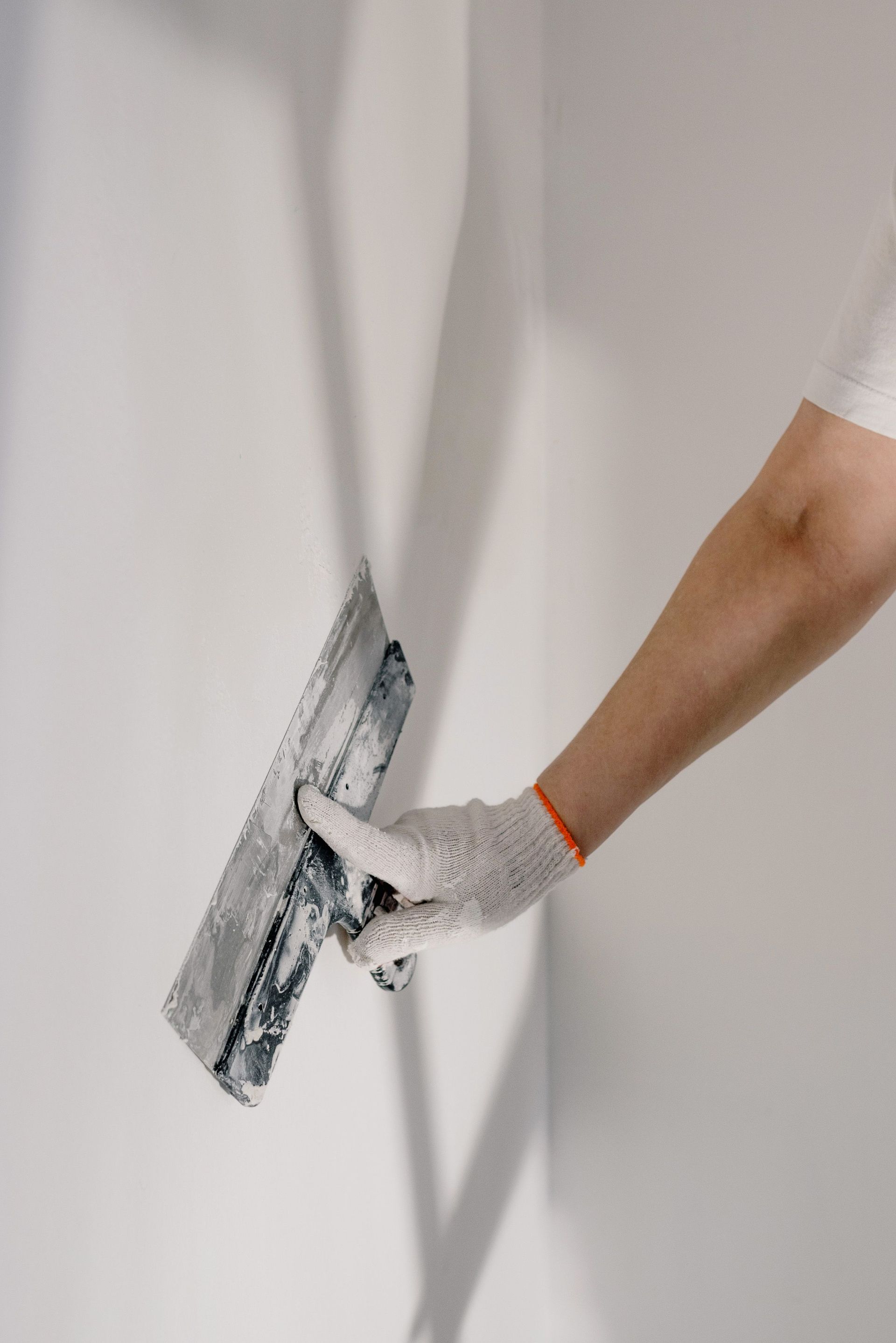 Una mano enguantada alisa la pintura blanca de una pared con una espátula.