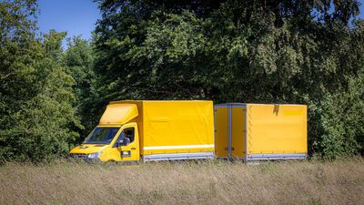 Ein gelber Lieferwagen parkt im hohen Gras neben dichten grünen Bäumen.