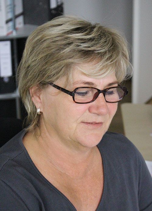 Frau mit Brille und blonden Haaren, die nach unten schaut und ein graues Hemd trägt.