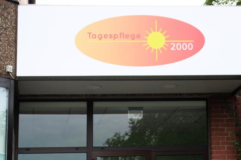 Schild der Tagespflege 2000 mit ovalem Logo mit Sonne in warmen Farben.