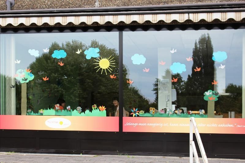 Schaufensterdekoration mit Papierausschnitten von Bäumen, Sonne, Wolken und Blumen.