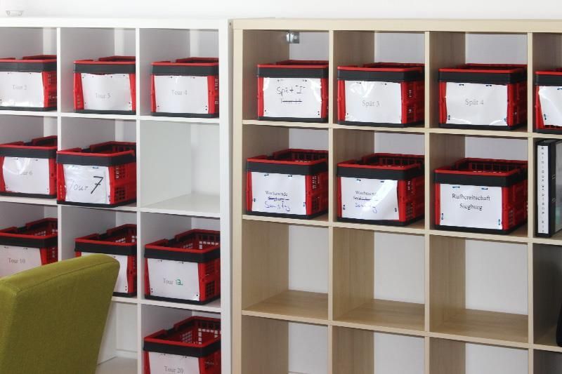 Regale mit rot und schwarz beschrifteten Behältern in einem Klassenzimmer.
