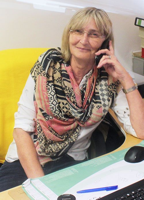 Frau mit Brille telefoniert am Schreibtisch und trägt einen Schal.