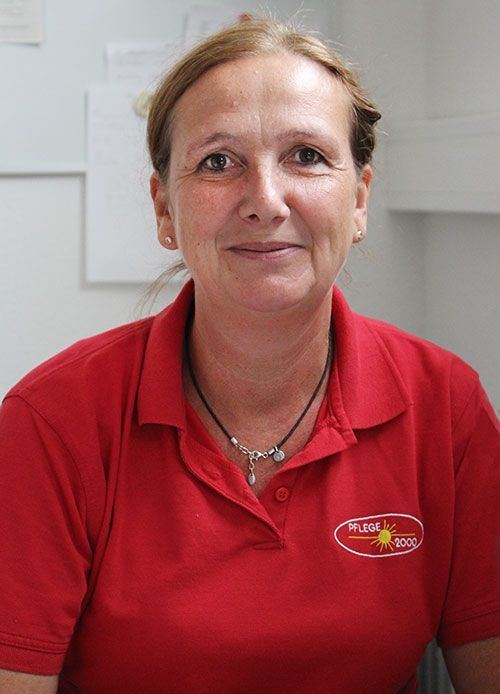 Frau mit blonden Haaren und rotem Poloshirt lächelt in die Kamera.