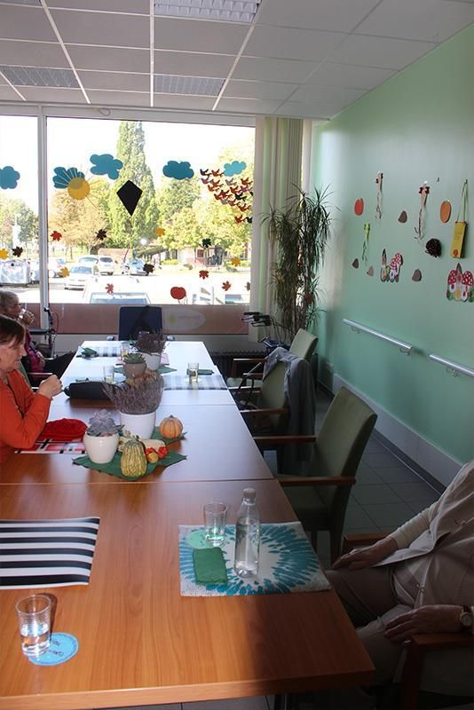 Menschen sitzen an einem langen Tisch in einem Raum mit einem großen Fenster. Dekorationen schmücken das Fenster und die Wand.