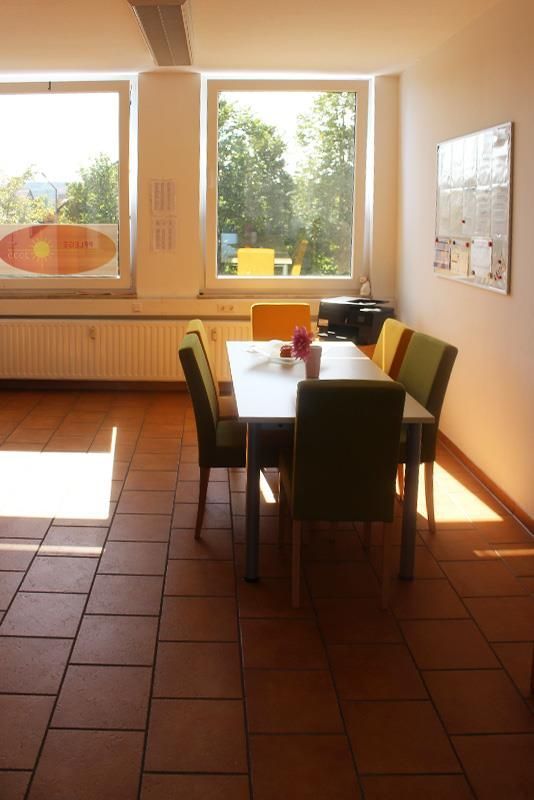 Esszimmer mit Tisch und Stühlen, Fenstern mit Sonnenlicht und Blick auf Bäume.