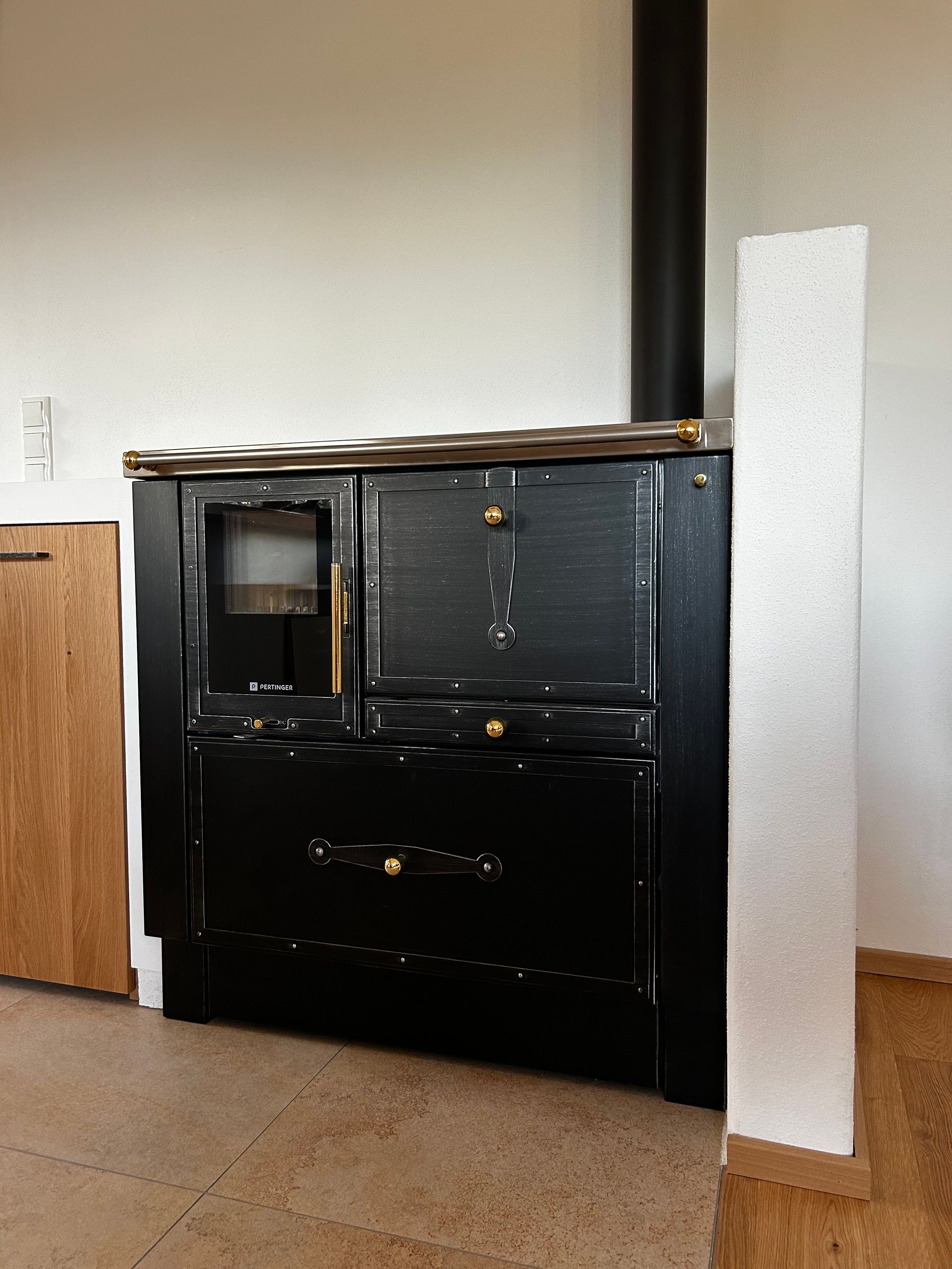 Schwarzer Küchenherd mit Messingakzenten in einem Raum mit hellem Holz und einer weißen Wand.