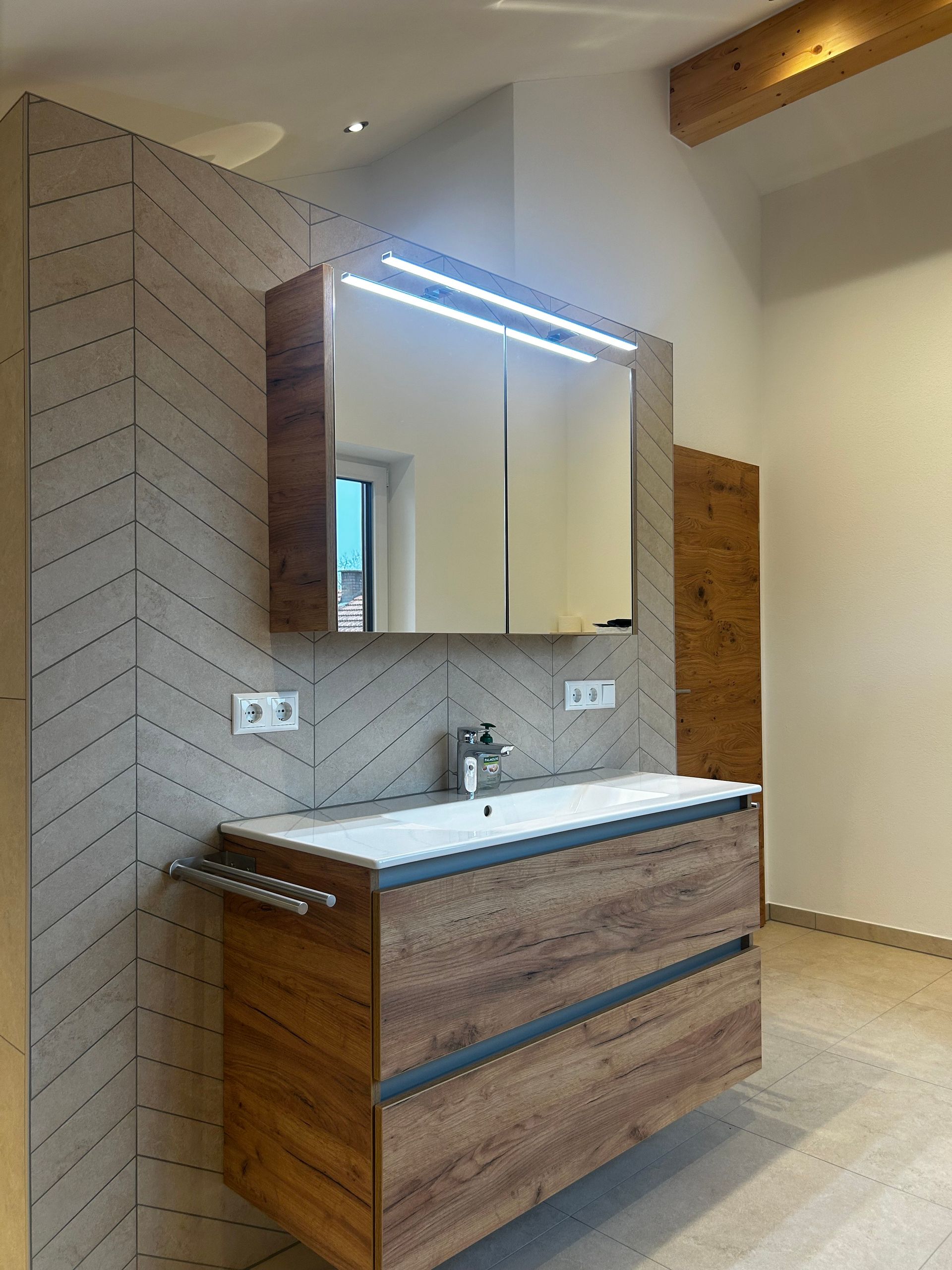 Badezimmer mit Waschtisch aus Holz, Spiegelschrank und gemusterter Fliesenwand.