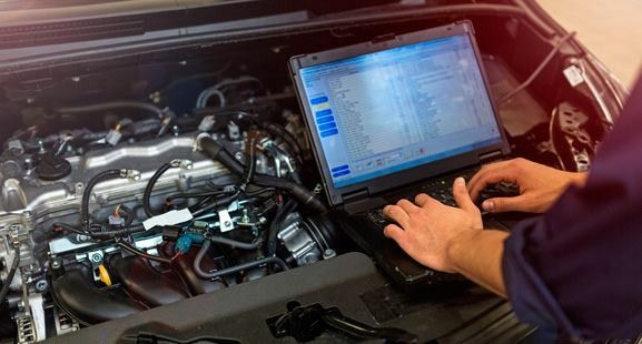 Un mecánico está usando una computadora portátil para revisar el motor de un automóvil.