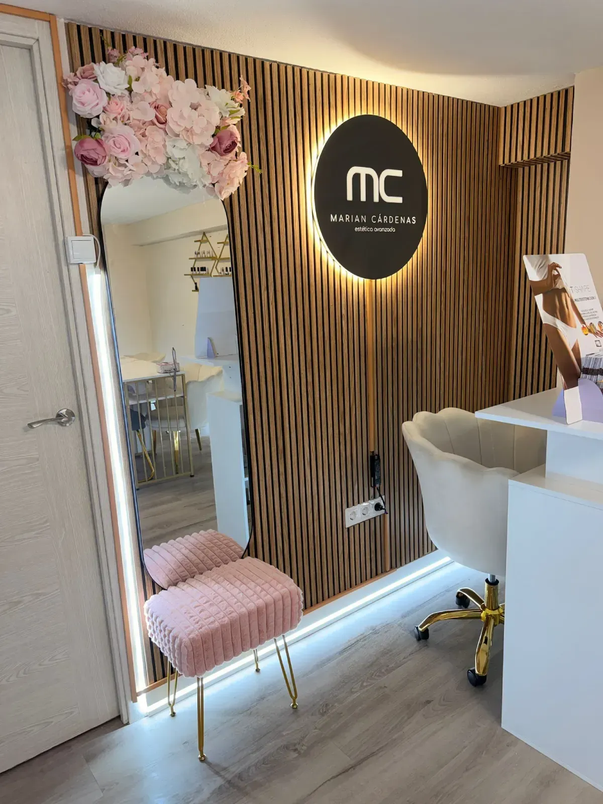 Un rincón acogedor con un sillón rosa, una mesita auxiliar dorada, un carrito blanco de varios niveles y carteles