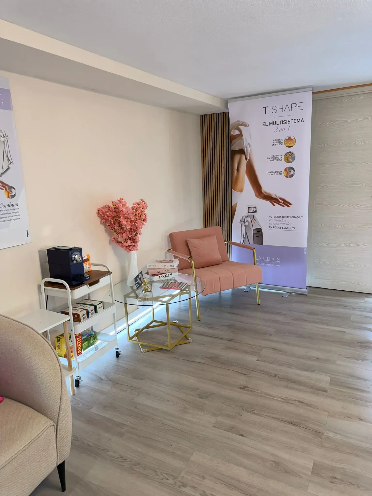 Un rincón acogedor con un sillón rosa, una mesita auxiliar dorada, un carrito blanco de varios niveles y carteles