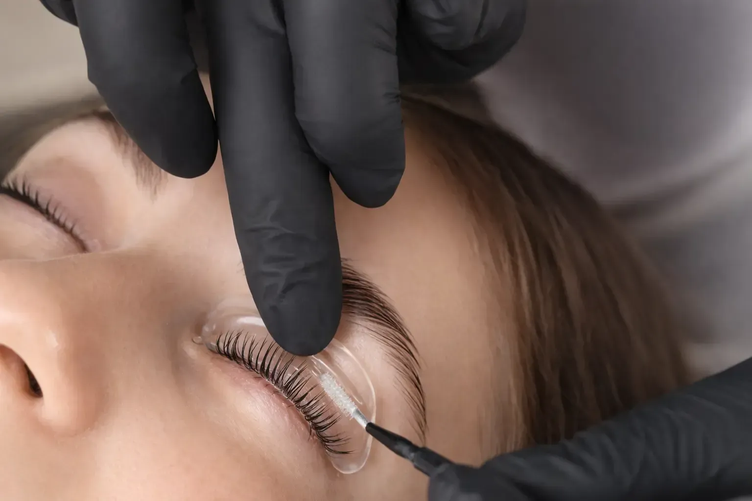 Un técnico con guantes aplica una varilla de silicona para levantar las pestañas, sujetando así las pestañas naturales
