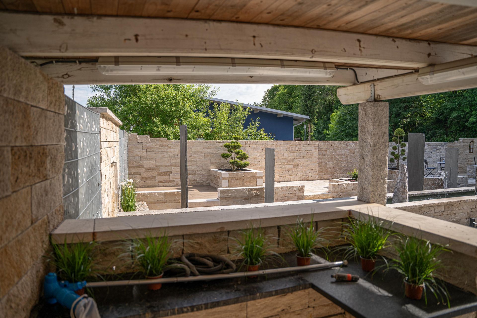 Überdachter Gartenbereich mit Natursteinmauern, Holzdecke und integrierter Bepflanzung