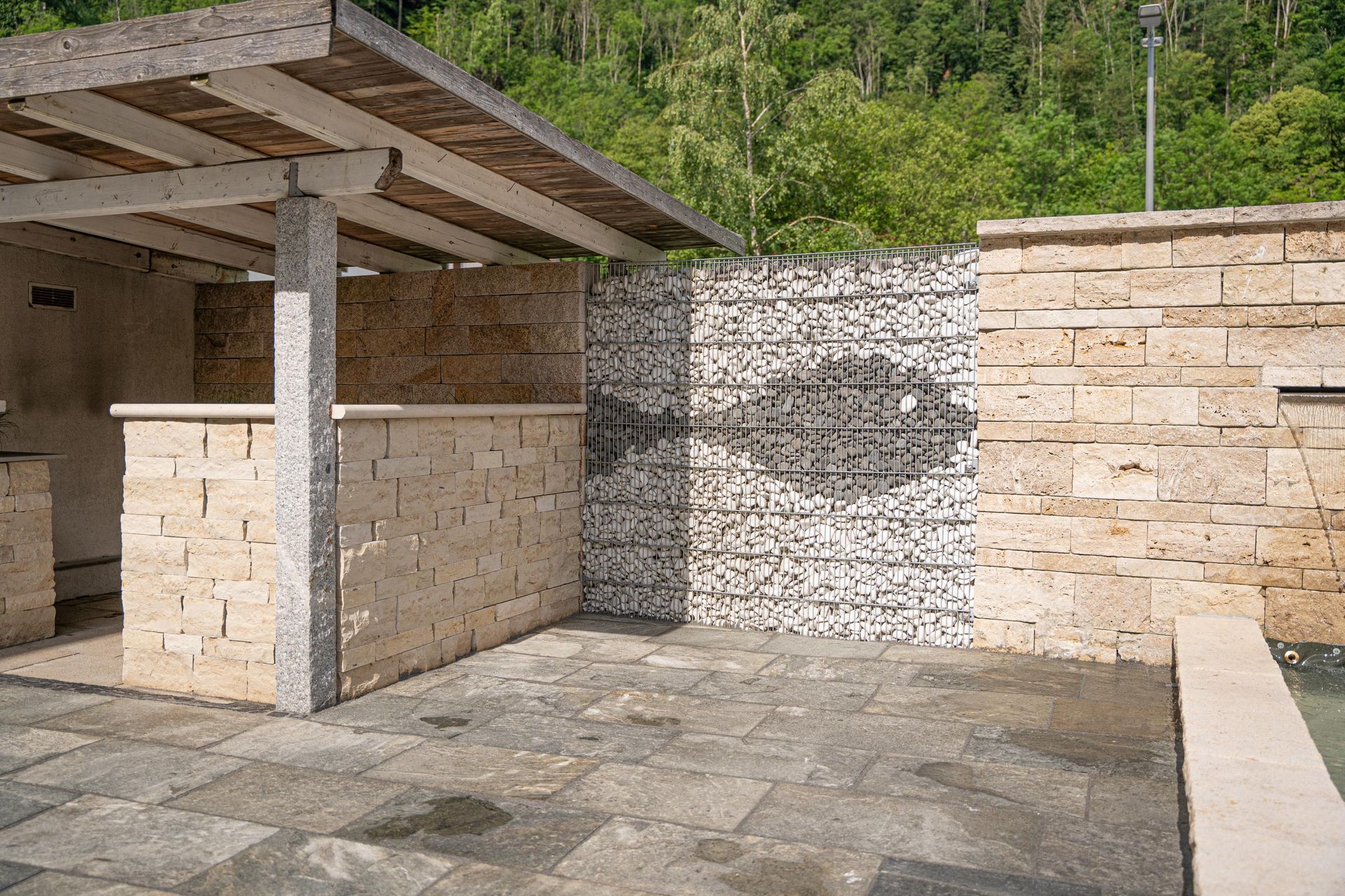 Terrasse mit Natursteinmauern, Pergola und strukturierter Steinwand