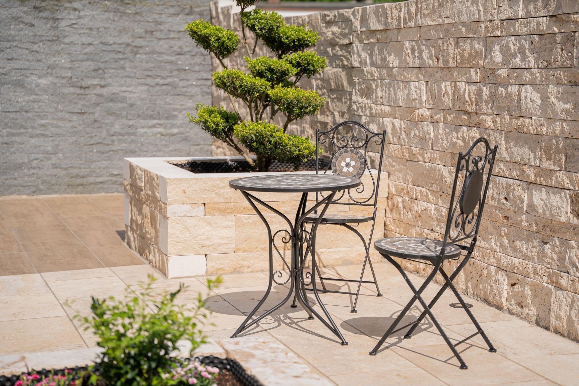 Terrasse mit Natursteinmauer, Sitzgruppe und formgeschnittenem Zierbaum
